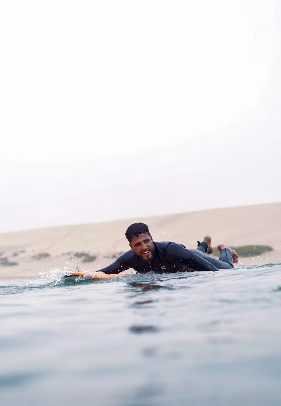 Surfer smiling while paddling on a surfboard in the Moroccan water