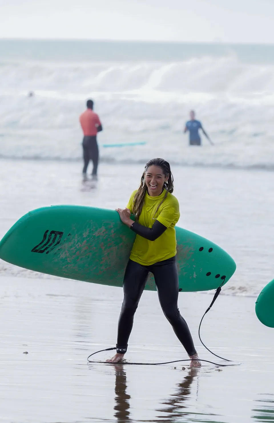Surf camp guest smiling warmly while carrying a board along the shoreline